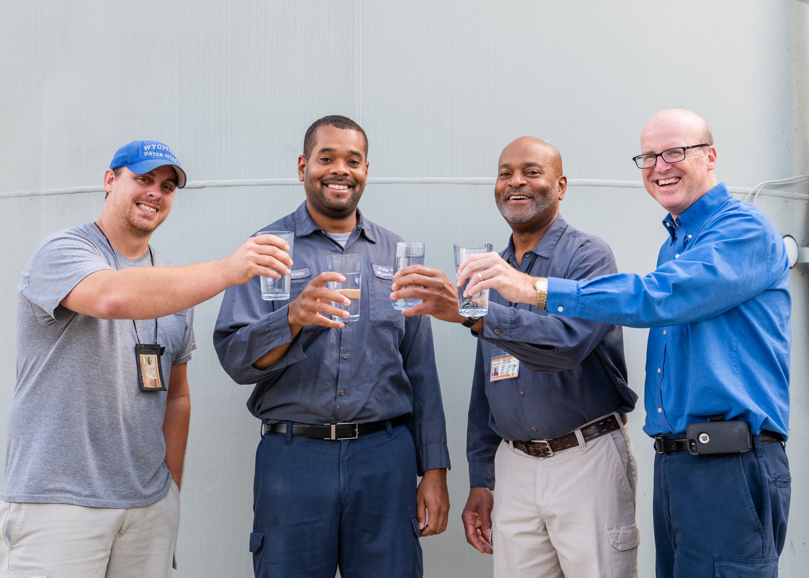 4 men holding cups filled with water up and smiling. 